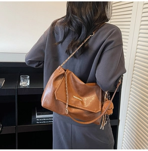 Detailed view of brown leather shoulder bag with gold chain and cute plush bear charm