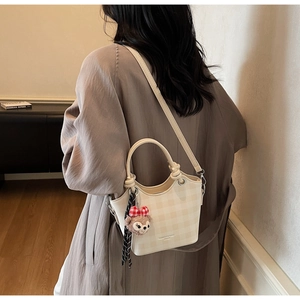 Detailed close-up of cream plaid bucket bag featuring a plush bear charm and silk ribbon