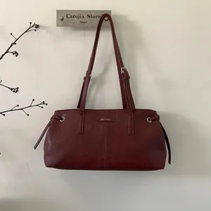 Dettaglio della borsa tote in pelle bordeaux con cinghie regolabili e logo in metallo