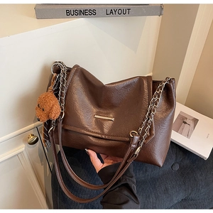 Detail view of brown pleated leather shoulder bag with gold chain and plush bear charm