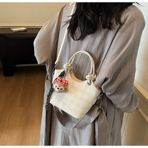 Detail view of beige checkered crossbody bag with knotted handle and plush charm