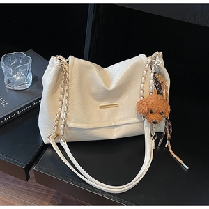 Detail of cream white faux leather tote bag featuring gold hardware and teddy bear charm