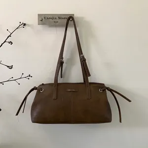 Dettaglio borsa a tracolla in pelle marrone retrò con fibbie argentate e logo metallico