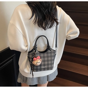 Detailed close-up of a grey plaid bucket bag with a plush charm on a wooden staircase
