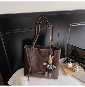 Dettaglio borsa tote marrone vintage con ciondolo a coniglio su un lenzuolo bianco
