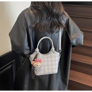 Detail of plaid shoulder bag with plush charm on a model wearing a black leather coat
