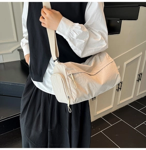 Close-up of light beige nylon cylinder bag with wide canvas strap on model in stairs