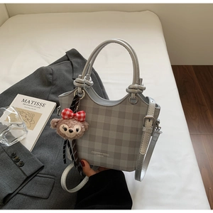 Detail view of grey plaid handbag with elegant ring handle and plush bear charm