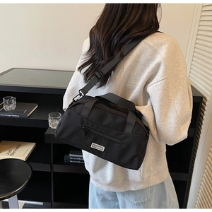 Rear view of a model wearing a black nylon Boston bag with a wide adjustable shoulder strap