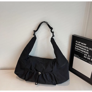 Detail of black nylon crescent tote bag showing side zipper pocket and drawstring texture