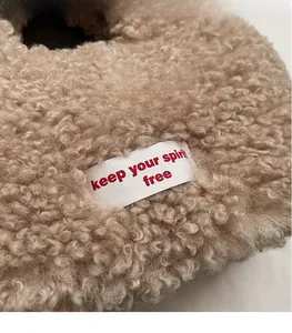 Detail of beige fleece tote bag featuring a white slogan patch and soft curly wool texture