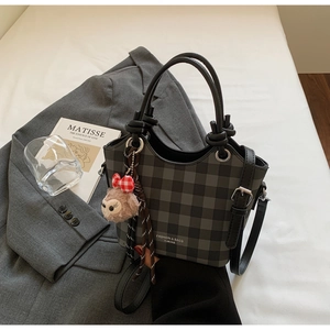 Close-up of checkered handbag with decorative knot handles and cute plush charm pendant