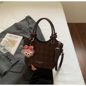 Detail view of brown checkerboard tote bag featuring a plush doll charm and double handles