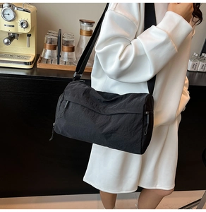 Detail of black nylon cylinder crossbody bag with wide strap on casual white outfit