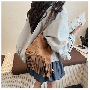 Detailed view of a brown suede shoulder bag with bohemian long fringe and slim strap
