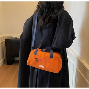 Detail of trendy orange canvas pillow bag with navy blue straps and front zipper pocket