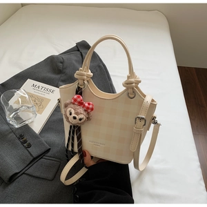Detail of a creamy checkered bucket bag with a plush bear charm and adjustable strap