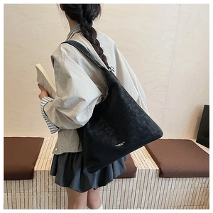 Détail d'un grand sac cabas noir vintage en daim avec lettrage porté à l'épaule