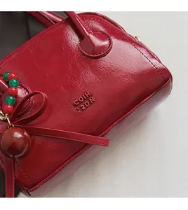 Détail du sac polochon rouge en cuir huilé avec texte COIH 12DN et pendentif à perles