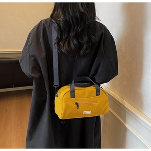 Detail of a bright yellow pillow bag with a black handle and stylish fashion label
