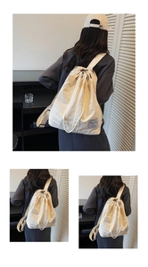 Detail view of the beige nylon drawstring backpack showing adjustable straps and round base