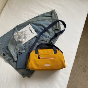 Detail of a yellow crossbody pillow bag with navy straps and front zipper pocket