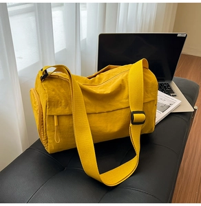 Detail of mustard yellow gym bag on leather bench showing side zipper and nylon texture