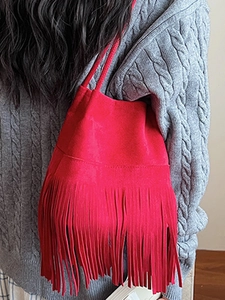 Red faux suede fringed bucket bag worn over shoulder with long flowing tassels
