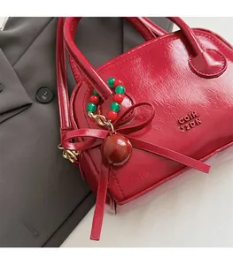 Détail du sac polochon rouge verni avec logo embossé et pendentif cerise sur costume