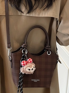 Brown checkered handbag with plush charm and detachable strap on khaki trench coat
