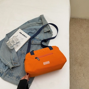 Detail of orange nylon pillow bag with blue adjustable strap and front zipper pocket