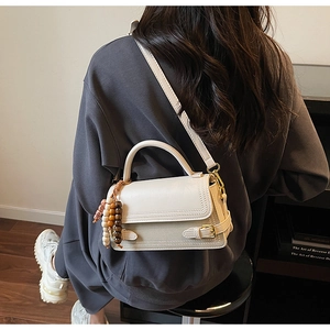 Detail view of cream shoulder bag featuring wooden bead charm and adjustable strap