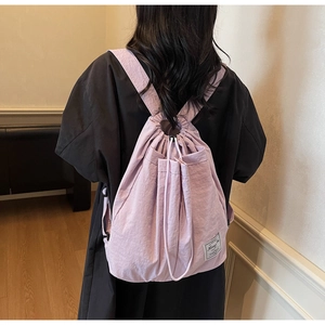 Rear view of a lilac drawstring backpack with front pocket on a model in a warm room