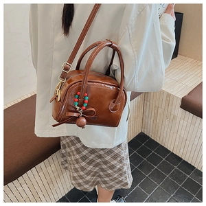 Détail d'un sac oreiller en cuir verni marron avec breloque nœud perlé et poignée ronde