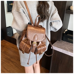 Detail of dark brown vintage PU leather backpack with gold buckles worn by model