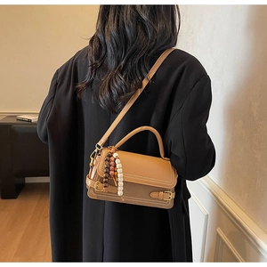 Detail view of brown leather handbag with vintage bead charm and adjustable shoulder strap