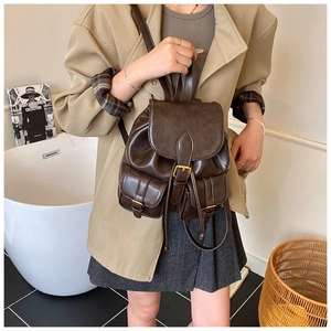 Detail showing deep brown faux leather backpack worn by model in minimalist indoor setting