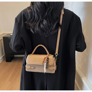 Detail of tan leather crossbody bag with colorful wooden beads on the handle worn by model