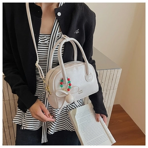 Détail du sac oreiller blanc avec breloques en perles colorées et nœud sur la bandoulière