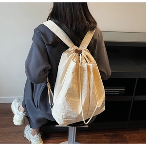 Detailed back view of a beige drawstring backpack with textured fabric and black buckles