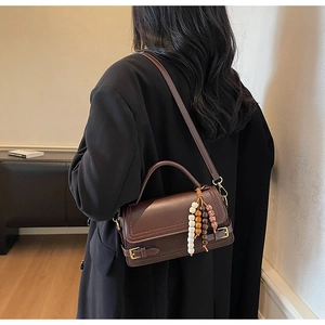 Detail of vintage dark brown crossbody bag with unique ethnic bead charm and leather texture
