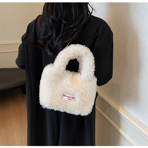 Detail of white plush sherpa tote bag with red lettered tag against a black coat