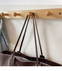 Detail of dark brown leather tote bag with long straps and zipper hanging on a hook