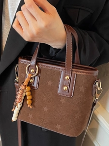 Brown suede bucket bag with star patterns, leather handle, and wooden bead charm accessory