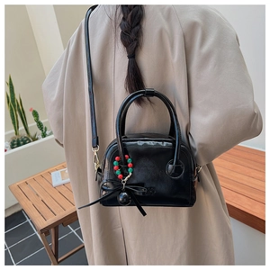 Détail du sac polochon noir brillant avec breloque perle verte et nœud papillon