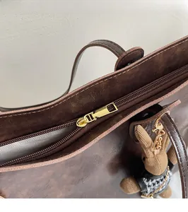 Detail of a dark brown tote bag showing smooth gold zipper hardware and plush rabbit charm