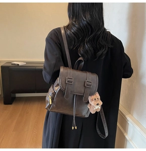 Detail eines dunkelbraunen Lederrucksacks mit Vintage-Schnalle und Plüsch-Anhänger
