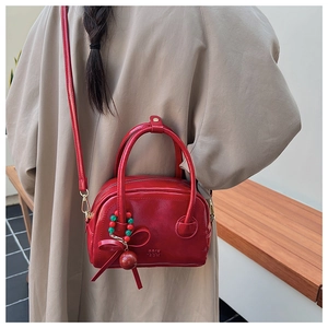 Détail d'un sac oreiller rouge vif avec un pendentif nœud perlé et une bandoulière fine