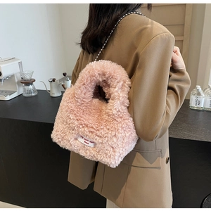 Model showcasing a pink plush tote bag with a silver ball chain strap in a cafe setting