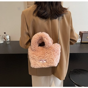 Detail of pink plush handbag with silver ball chain and white label worn by a model